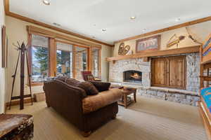 Living room featuring light carpet, a stone fireplace, and ornamental molding