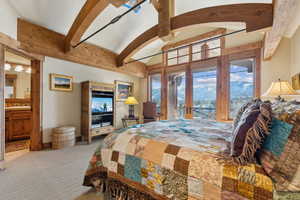 Bedroom with access to exterior, beam ceiling, ensuite bathroom, light carpet, and french doors