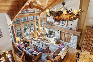 Living room featuring beam ceiling, a stone fireplace, wooden ceiling, and light hardwood / wood-style floors