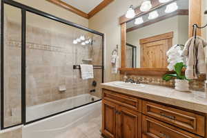 Bathroom featuring tile patterned floors, ornamental molding, shower / bath combination with glass door, and vanity