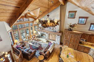 Living room with high vaulted ceiling, a stone fireplace, light hardwood / wood-style floors, and beam ceiling