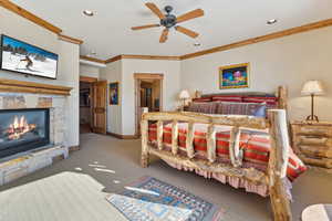 Carpeted bedroom featuring ceiling fan, ornamental molding, and a fireplace