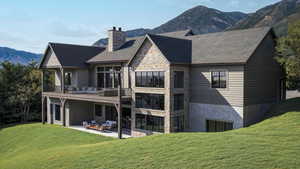 Rear view of house with a balcony, a mountain view, a yard, and a patio area