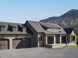 View of front of home with an attached garage, a mountain view, asphalt driveway, stone siding, and a chimney