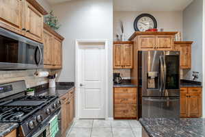 Kitchen with light tile patterned flooring, appliances with stainless steel finishes, and dark stone counters