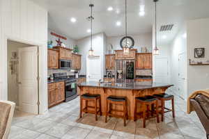 Kitchen featuring appliances with stainless steel finishes, a large island, decorative light fixtures, and a kitchen bar