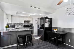 Kitchen with a breakfast bar, white cabinets, light stone counters, kitchen peninsula, and fridge with ice dispenser