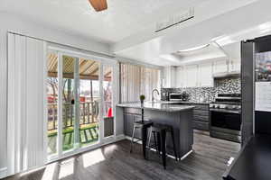 Kitchen with dark wood-type flooring, a breakfast bar, stainless steel appliances, white cabinets, and dark stone counters