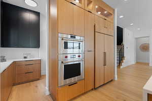 Kitchen with light wood finished floors, double oven, light countertops, baseboards, and modern cabinets