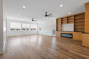 Unfurnished living room featuring a glass covered fireplace, recessed lighting, baseboards, a ceiling fan, and wood finished floors