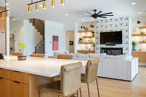 Kitchen featuring a breakfast bar area, ceiling fan, a center island, a fireplace, and light hardwood / wood-style floors