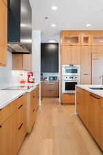 Kitchen featuring sink, light hardwood / wood-style flooring, double oven, ventilation hood, and black electric cooktop