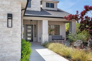 Doorway to property featuring covered porch, stone siding, and stucco siding