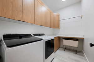 Clothes washing area featuring separate washer and dryer, light hardwood / wood-style flooring, and cabinets