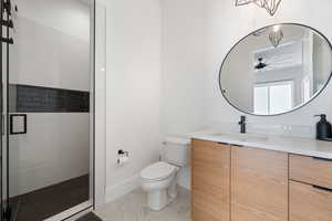 Bathroom featuring ceiling fan, vanity, toilet, and an enclosed shower