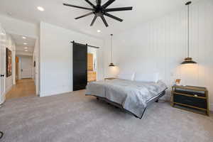 Carpeted bedroom featuring a barn door and ceiling fan