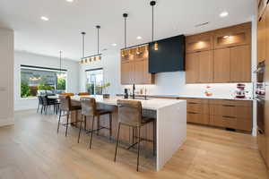 Kitchen with sink, a kitchen island with sink, hanging light fixtures, a kitchen breakfast bar, and range hood