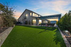 Back house at dusk featuring a pergola and a lawn