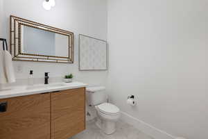 Bathroom with vanity, baseboards, toilet, and marble finish floor