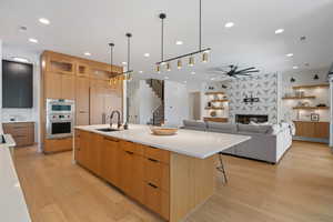 Kitchen with ceiling fan, modern cabinets, light wood-type flooring, a spacious island, and a sink