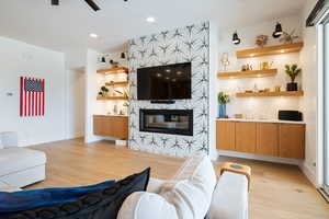 Living room with ceiling fan, a tiled fireplace, and light hardwood / wood-style flooring