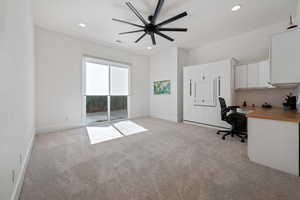 Unfurnished office with built in desk, light colored carpet, and ceiling fan