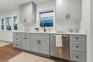 Kitchen with sink, light hardwood / wood-style flooring, stainless steel dishwasher, gray cabinets, and a healthy amount of sunlight