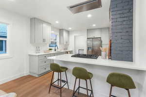 Kitchen featuring light hardwood / wood-style flooring, appliances with stainless steel finishes, a kitchen breakfast bar, gray cabinets, and kitchen peninsula