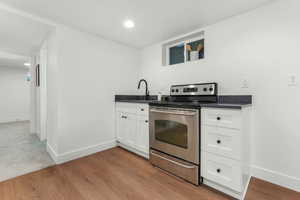 Kitchen with stainless steel electric stove, sink, white cabinets, and light hardwood / wood-style flooring