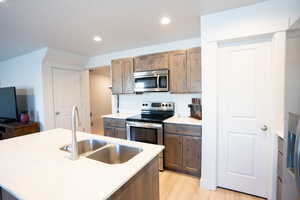 Kitchen with sink, stainless steel appliances, an island with sink, a textured ceiling, and light wood-type flooring