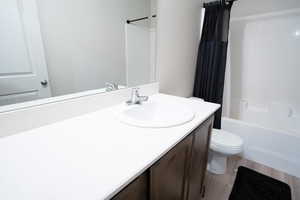 Full bathroom featuring shower / bath combination with curtain, vanity, toilet, and hardwood / wood-style flooring