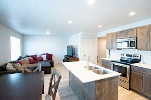 Kitchen featuring appliances with stainless steel finishes, an island with sink, sink, light wood-type flooring, and a textured ceiling