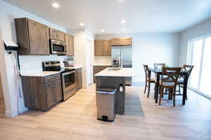 Kitchen with sink, a textured ceiling, a center island with sink, light hardwood / wood-style flooring, and appliances with stainless steel finishes