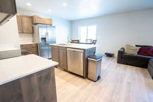 Kitchen featuring sink, light hardwood / wood-style flooring, appliances with stainless steel finishes, a textured ceiling, and a center island with sink