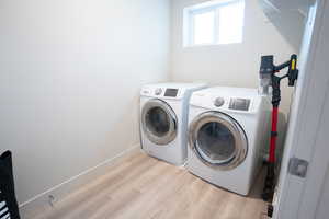 Clothes washing area with light hardwood / wood-style floors and washing machine and dryer