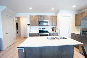 Kitchen featuring appliances with stainless steel finishes, sink, light hardwood / wood-style floors, and a kitchen island with sink