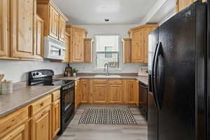 Kitchen with sink, light brown cabinets, light hardwood / wood-style floors, and black appliances