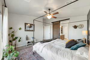 Carpeted bedroom featuring ceiling fan, connected bathroom, and a barn door