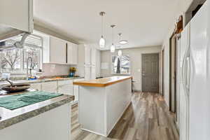 Kitchen with a kitchen island, white refrigerator with ice dispenser, white cabinets, and decorative light fixtures