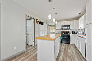 Kitchen featuring sink, white cabinetry, a center island, black appliances, and decorative light fixtures