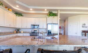 Kitchen featuring sink, white cabinetry, appliances with stainless steel finishes, a kitchen breakfast bar, and light stone countertops