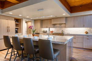 Kitchen with a breakfast bar, an island with sink, light stone countertops, light brown cabinets, and light hardwood / wood-style flooring