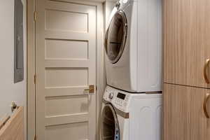 Laundry room with electric panel and stacked washer and clothes dryer