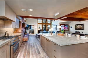 Kitchen featuring sink, stainless steel stove, light hardwood / wood-style flooring, backsplash, and a center island with sink