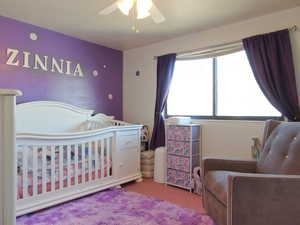 Carpeted bedroom featuring ceiling fan and a crib