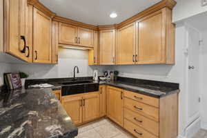 Kitchen featuring dark stone counters, sink, and light tile patterned floors