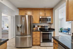 Kitchen featuring appliances with stainless steel finishes, light tile patterned floors, and dark stone counters