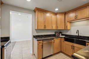 Kitchen with electric stove, sink, dishwasher, light tile patterned flooring, and dark stone counters