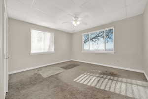 Carpeted spare room featuring a drop ceiling and ceiling fan