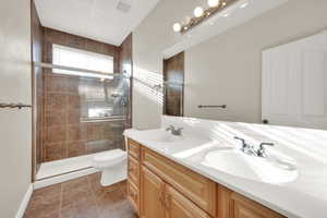 Bathroom with a shower with door, vanity, tile patterned flooring, and toilet